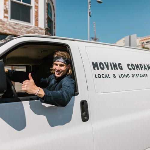 Smiling mover giving thumbs up from a moving company van parked outside.